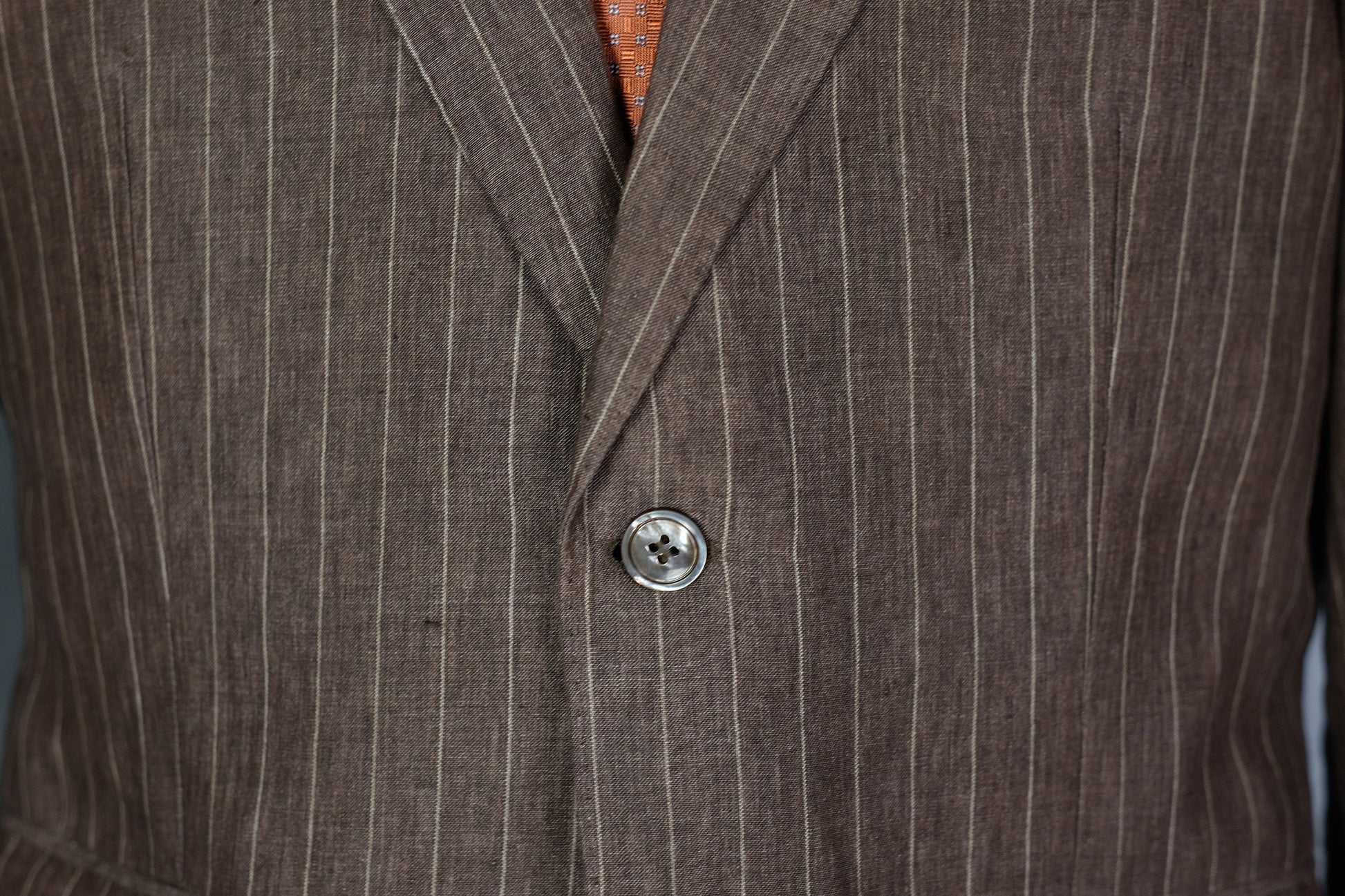Close-up of a brown pinstripe suit jacket with a button.