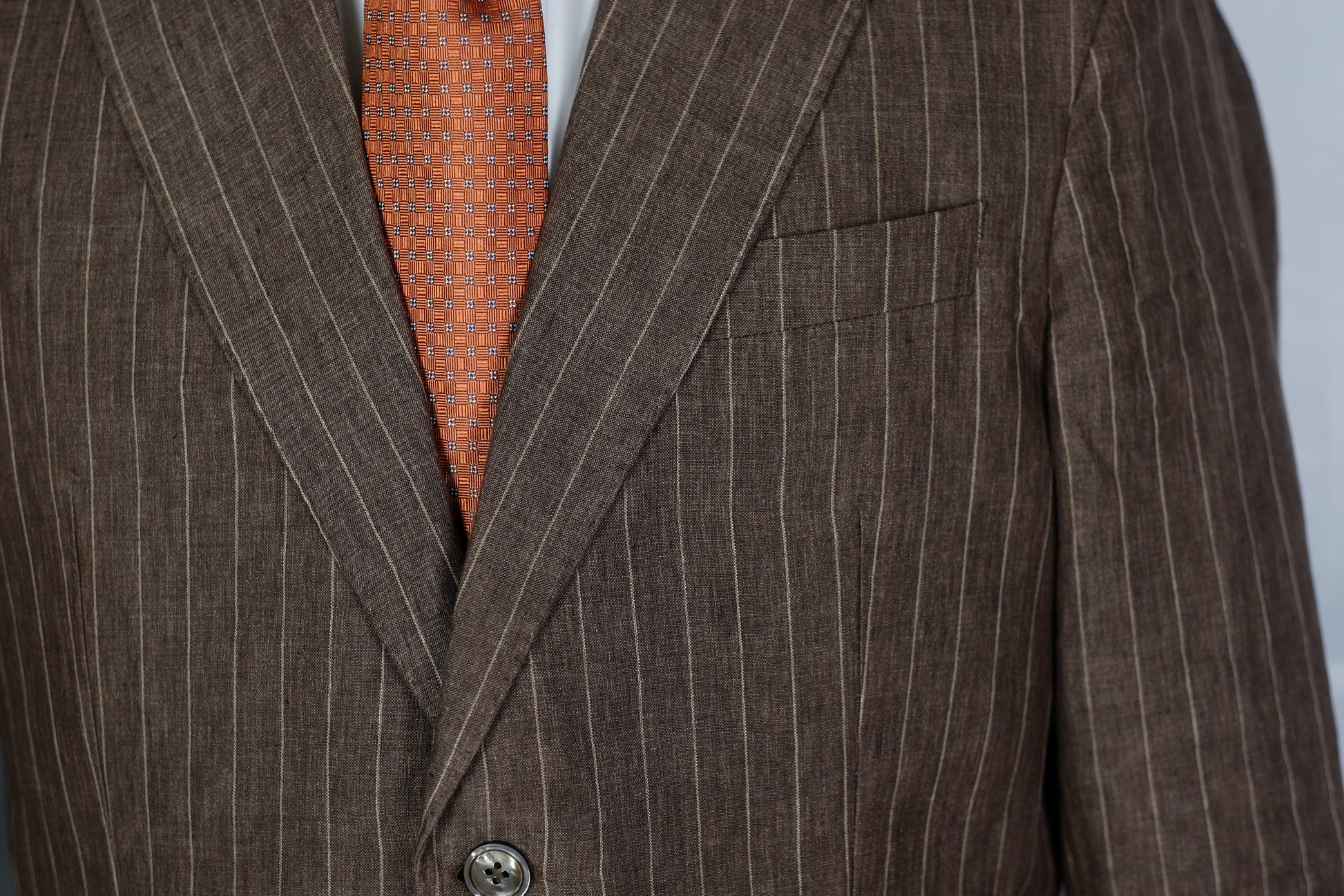 Brown pinstripe suit jacket with an orange patterned tie on a gray background