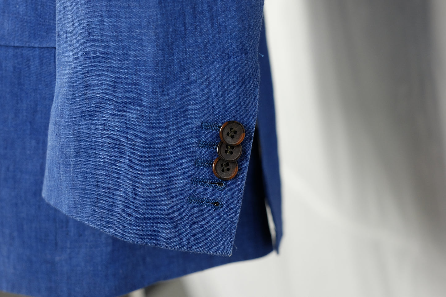 Close-up of a blue suit jacket with three buttons on a white background